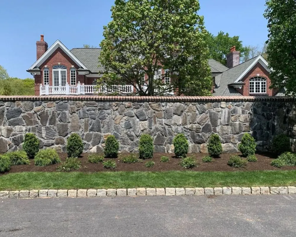 Custom stone retaining wall with garden bed and Belgian block curbing in Pound Ridge NY