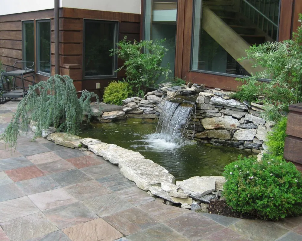Stone patio with integrated rock waterfall and pond design in Pound Ridge NY